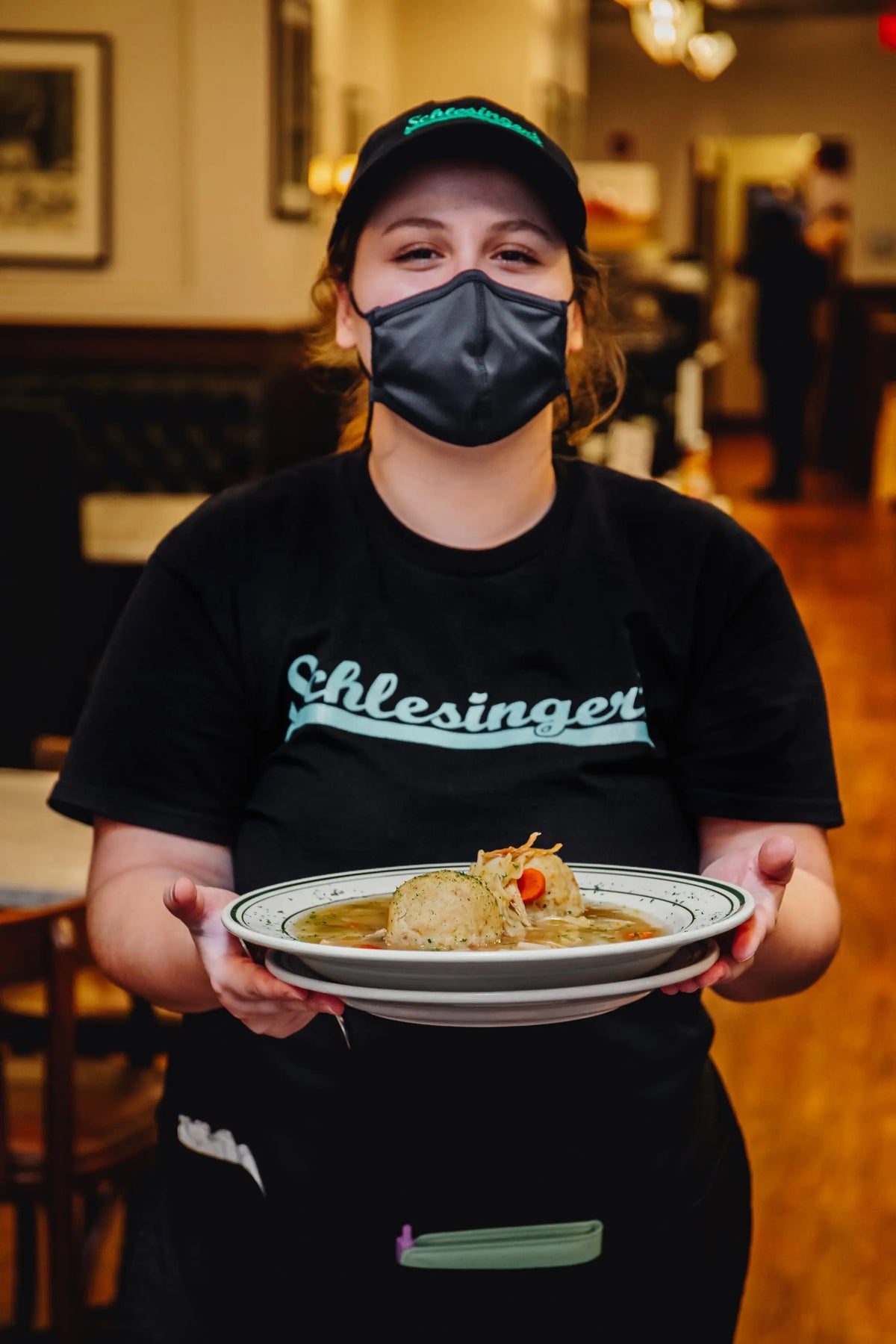 Person wearing a black 'Schlesingers' shirt holding a plate of food in a restaurant setting.