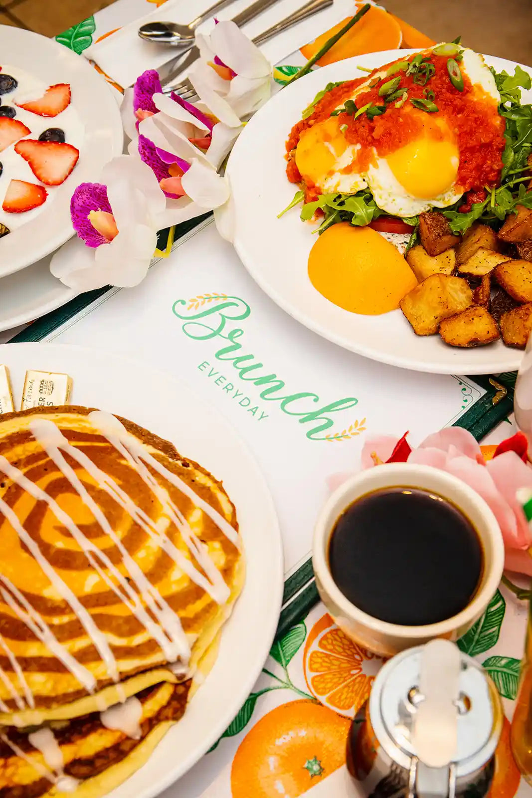 Brunch setting with pancakes, breakfast plate with pancakes, fruit bowl, coffee, and a colorful 'Brunch Everyday' placemat.