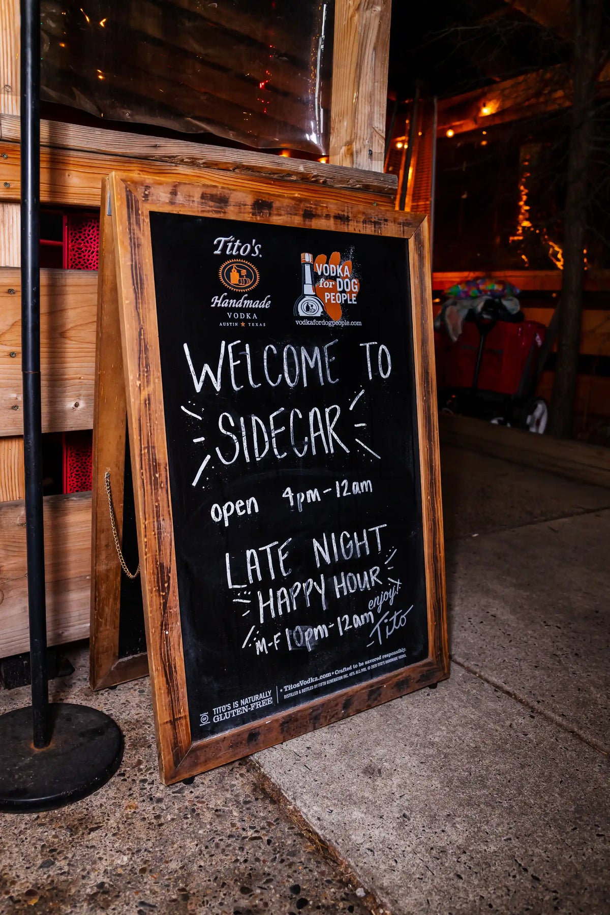 Wooden framed chalkboard sign outside a establishment named 'Sidecar' with opening hours and happy hour information.