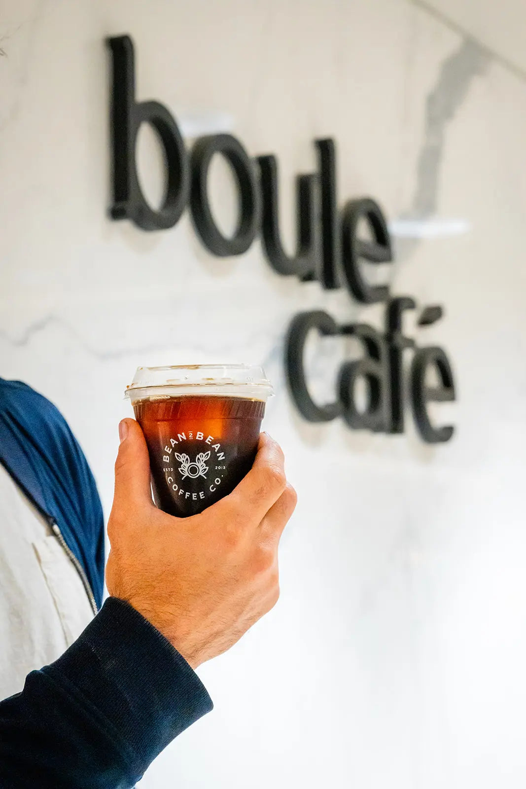 Hand holding a coffee cup in front of 'boule Cafe' sign