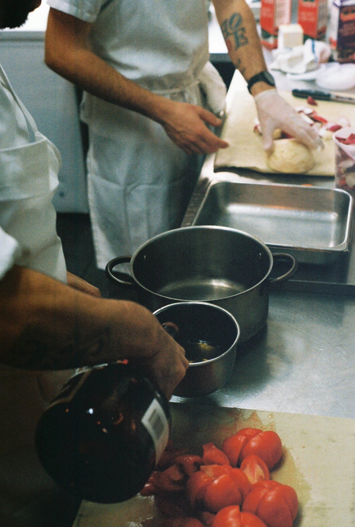 Person preparing food in a kitchen with pots and tomatoes on a counter.