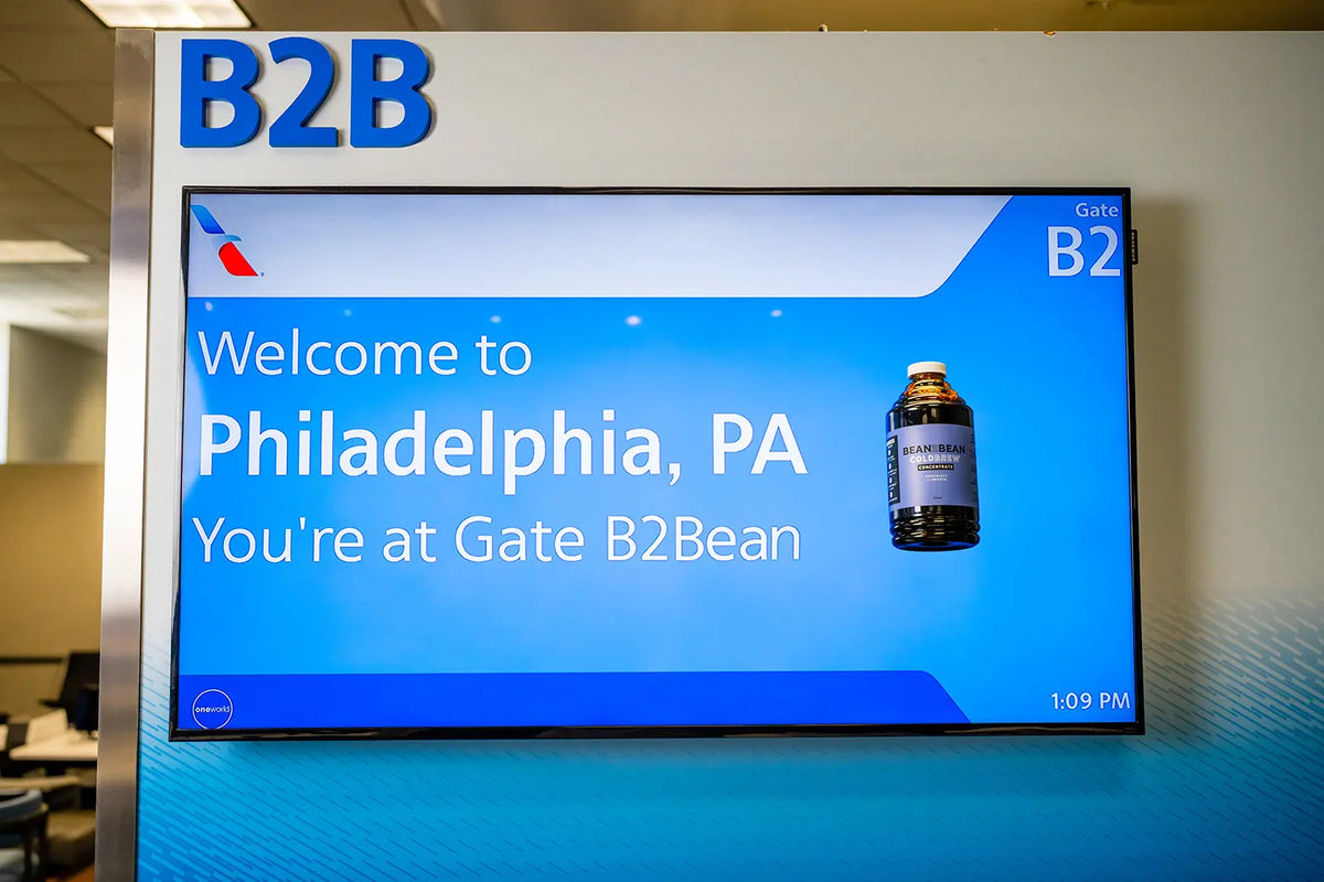 Gate "B2B" at Philadelphia International Airport that says "Welcome to Philadelphia, PA. You're at Gate Bean2Bean" with a Bean2Bean Cold Brew bottle floating on the screen