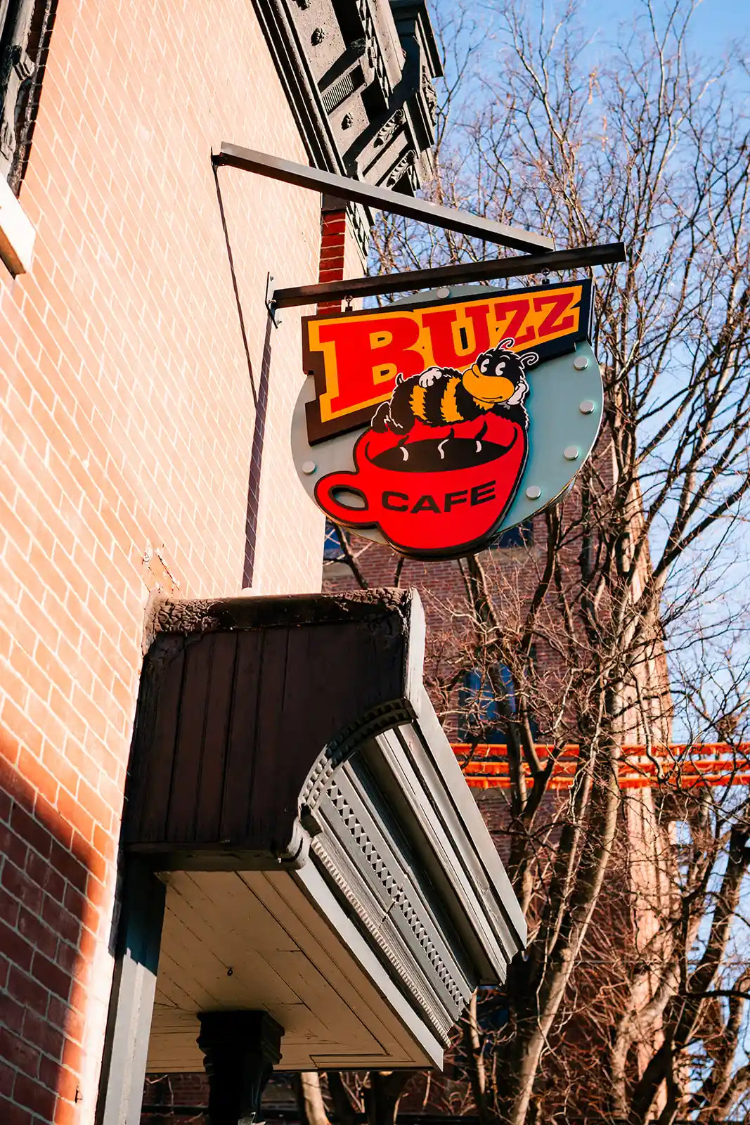 Buzz Cafe sign on a building exterior with trees and clear sky in the background
