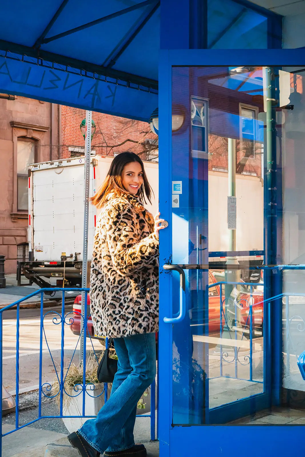 Woman in a leopard print coat standing in front of a Kanella Restaurant storefront in Philadelphia, PA