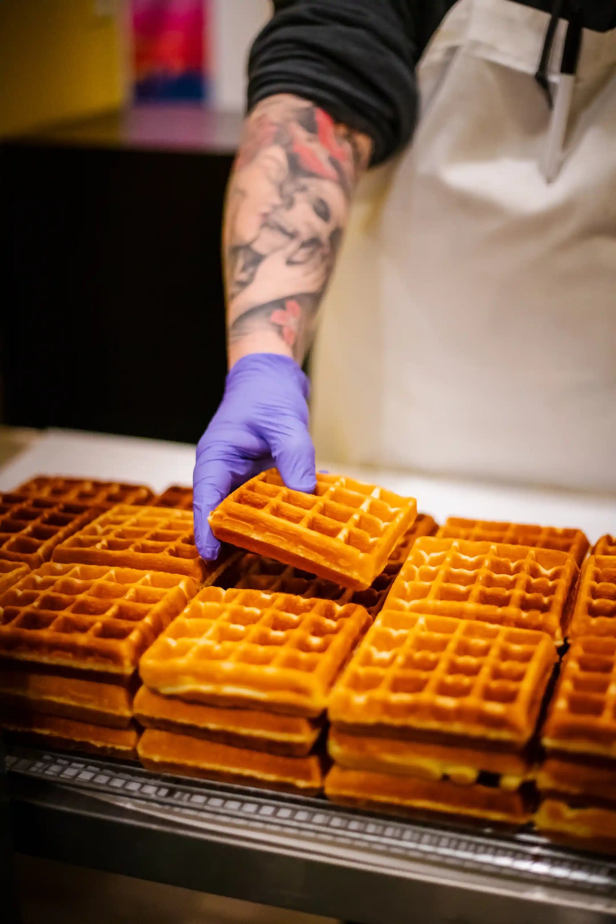 Person wearing a purple glove arranging waffles on a tray.