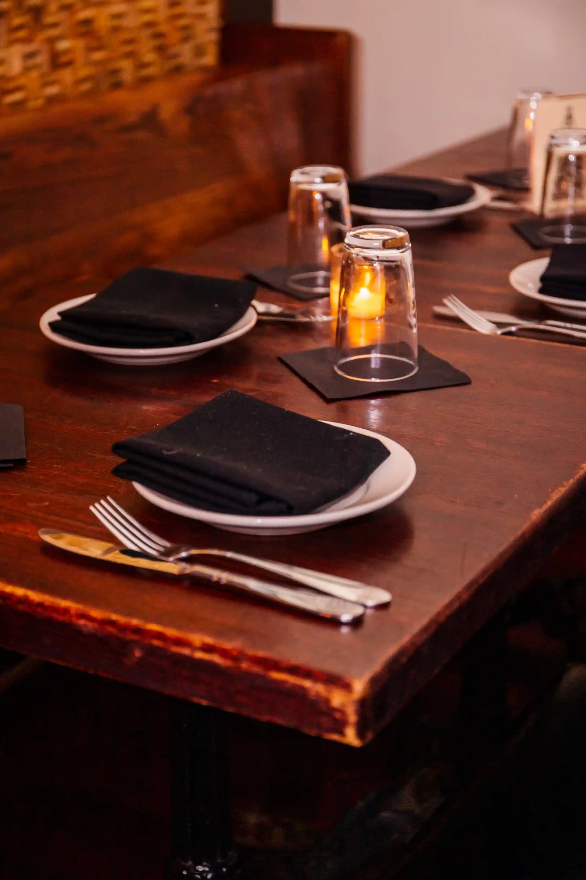 Dining table set with black napkins, white plates, and silverware in a dimly lit setting.