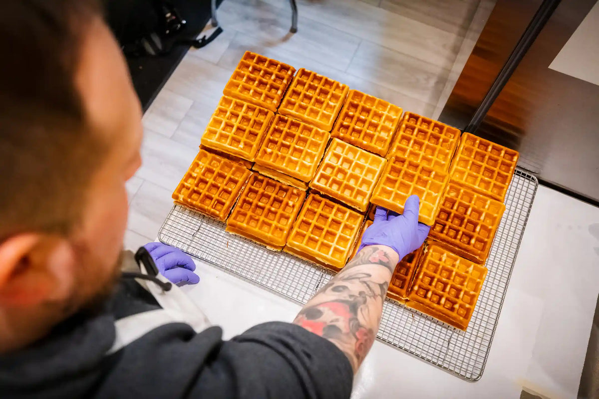 Person arranging freshly made waffles on a cooling rack in a kitchen.