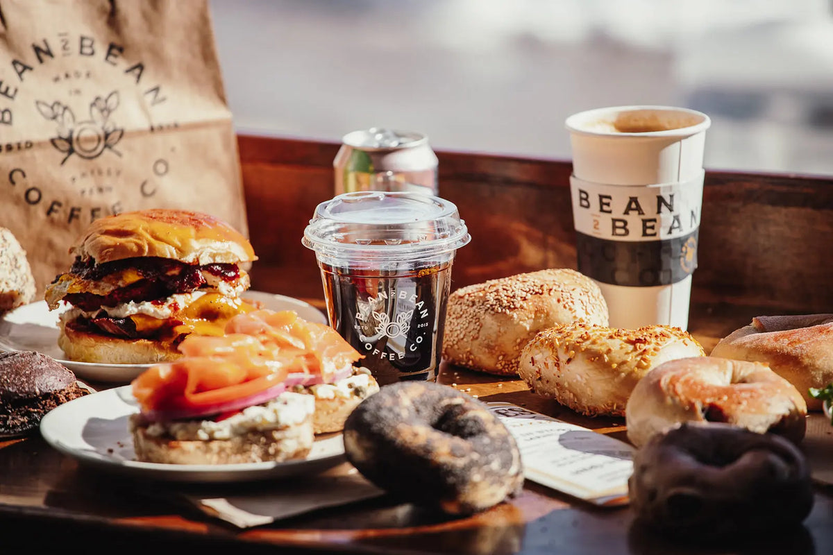 Table with food and drinks including a burger, donuts, Bean2Bean coffee, and a coffee cup with 'Bean2Bean' branding.