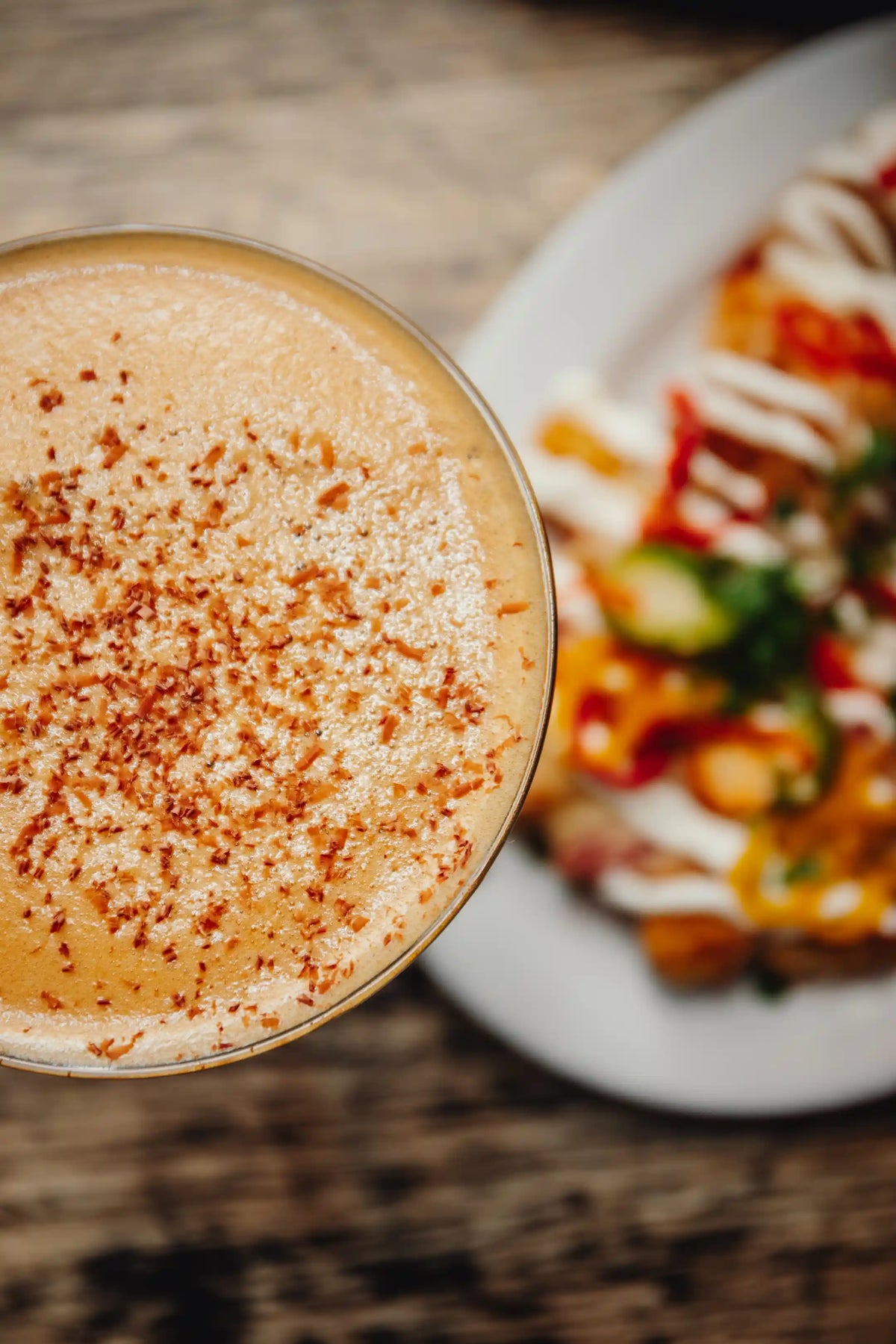 Close-up of a creamy Bean2Bean espresso martini with a textured surface, blurred plate of food in the background