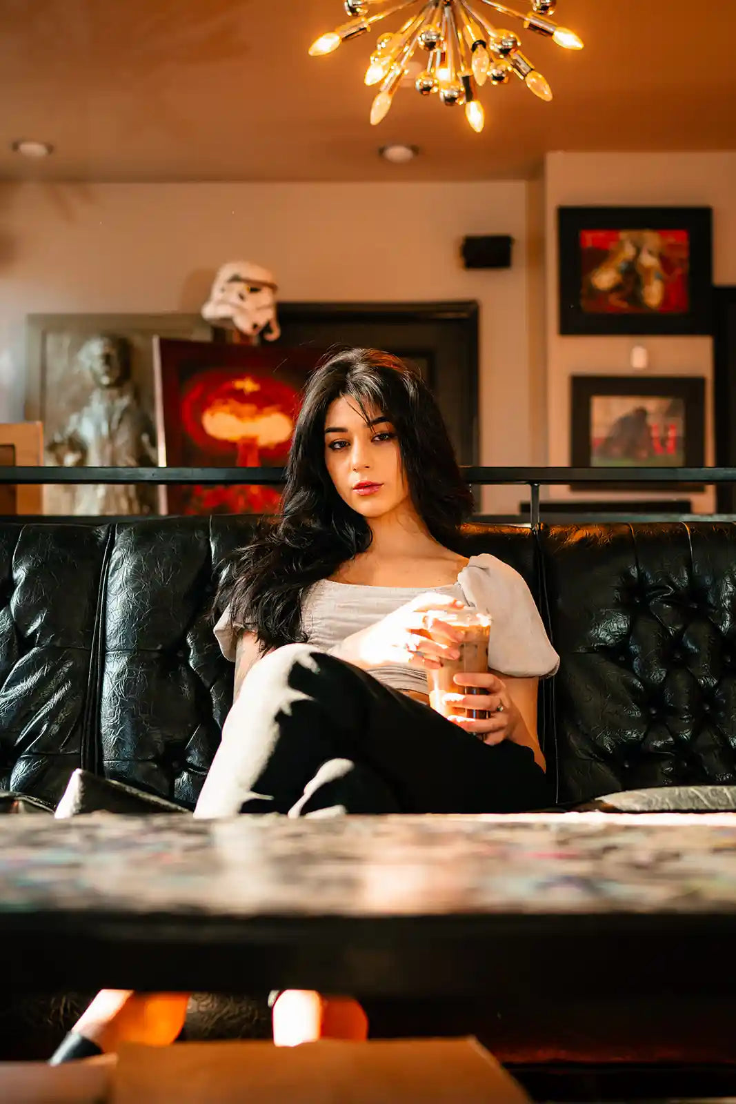 Woman sitting on a couch holding a drink in a cozy indoor setting.