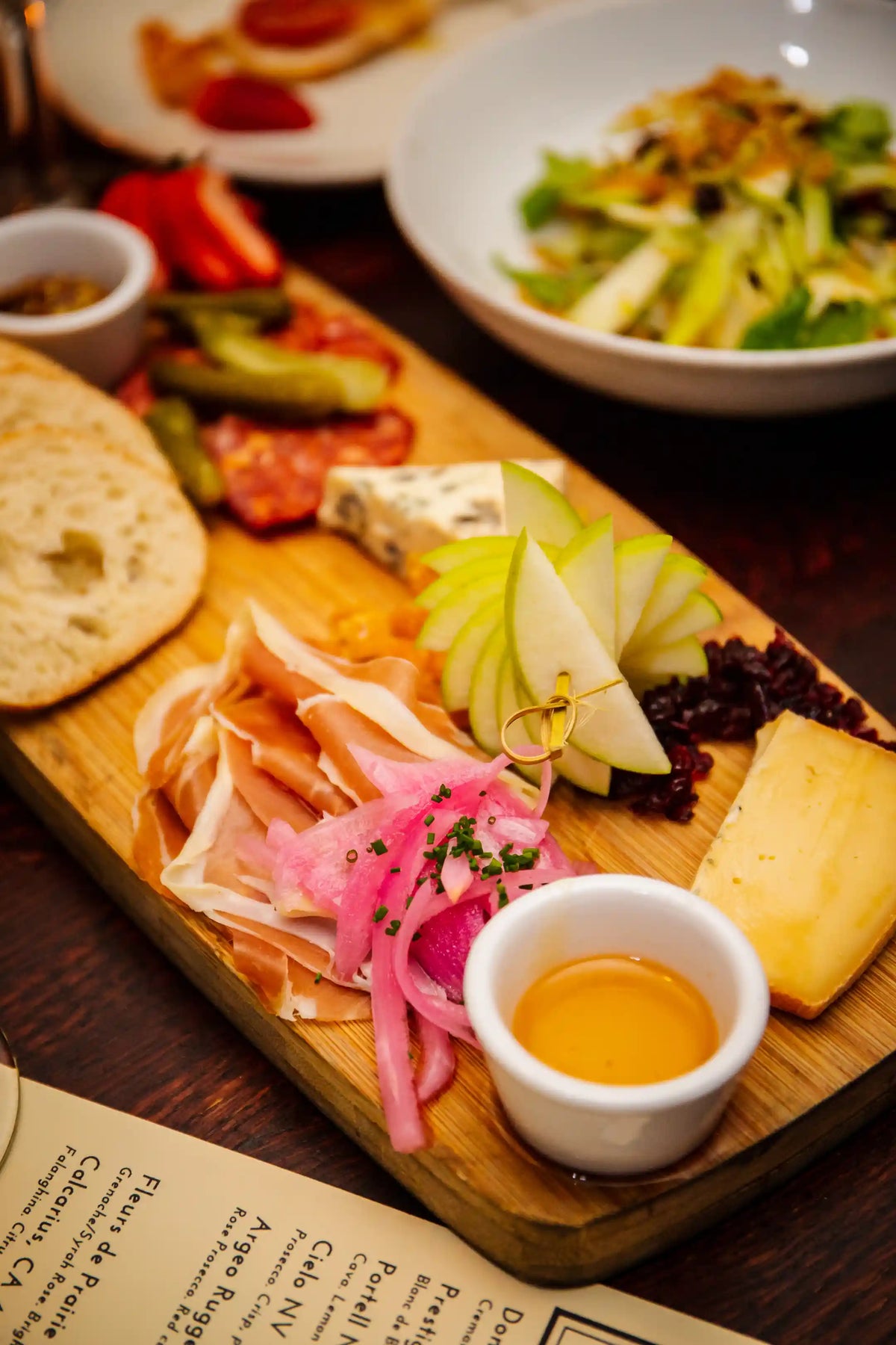 Wooden charcuterie board with cured meats, cheeses, and fruits on a dark surface.