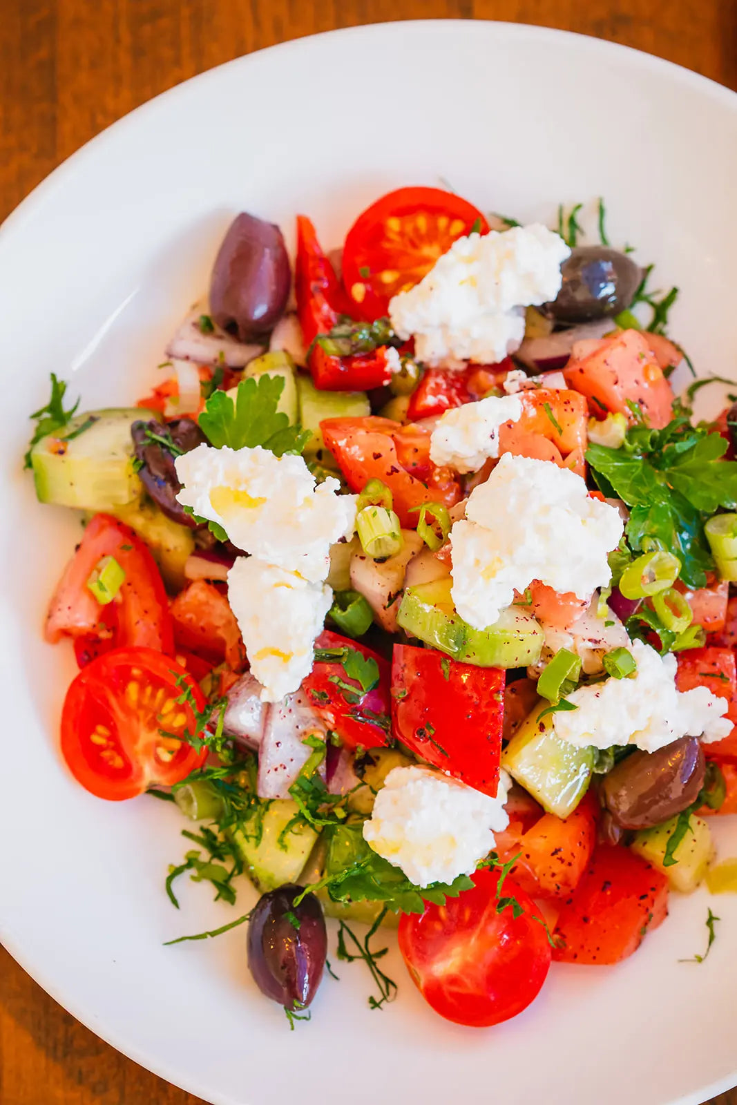 Colorful salad with tomatoes, cucumbers, olives, and feta cheese on a white plate.