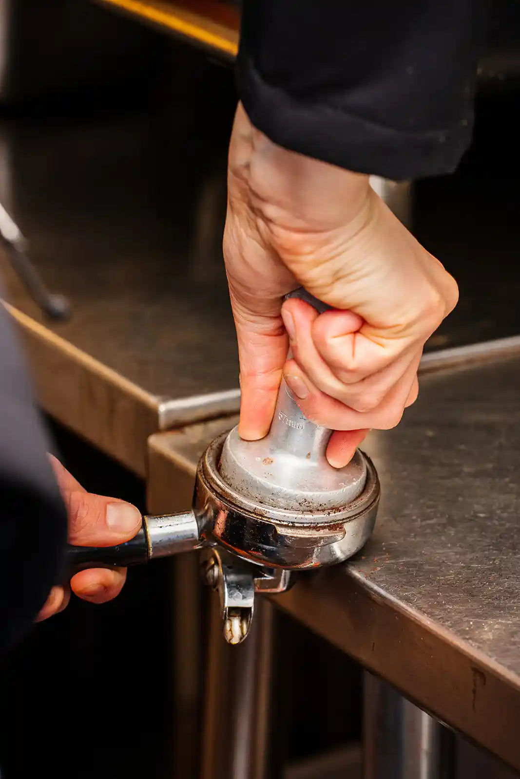 Hand using a coffee tamp to compress grounds in a portafilter.
