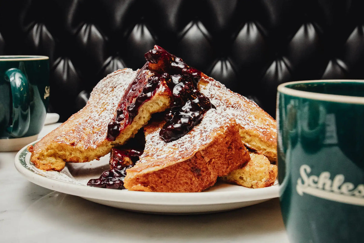 French toast with berry sauce on a plate with Schlesinger mugs in the background.