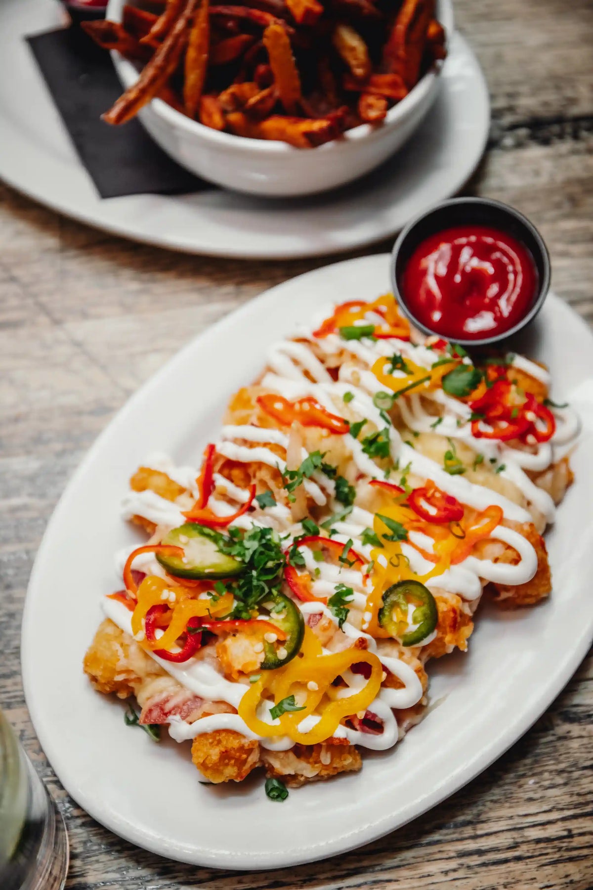 Plated dish of nachos on a wooden table with fries in background