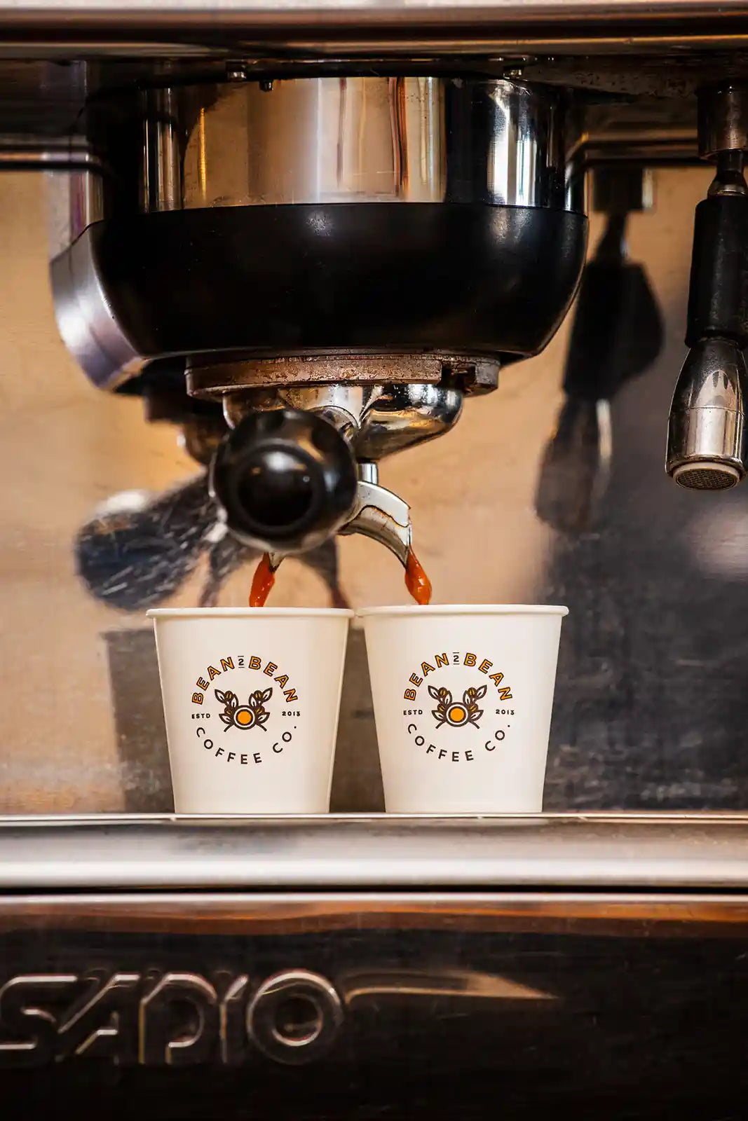 Espresso being poured into two mini Bean2Bean Coffee cups from a machine.