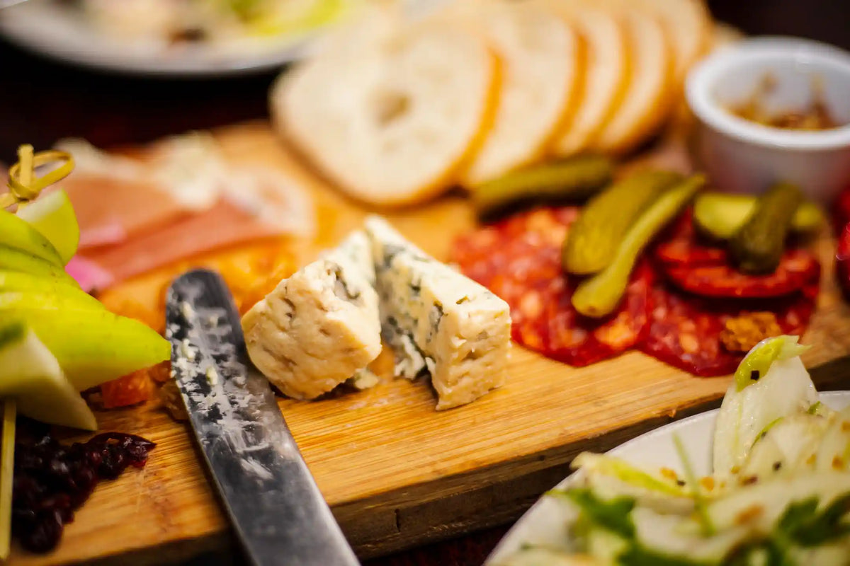Wooden cutting board with sliced bagels, cheese, and deli meats on a wooden table.