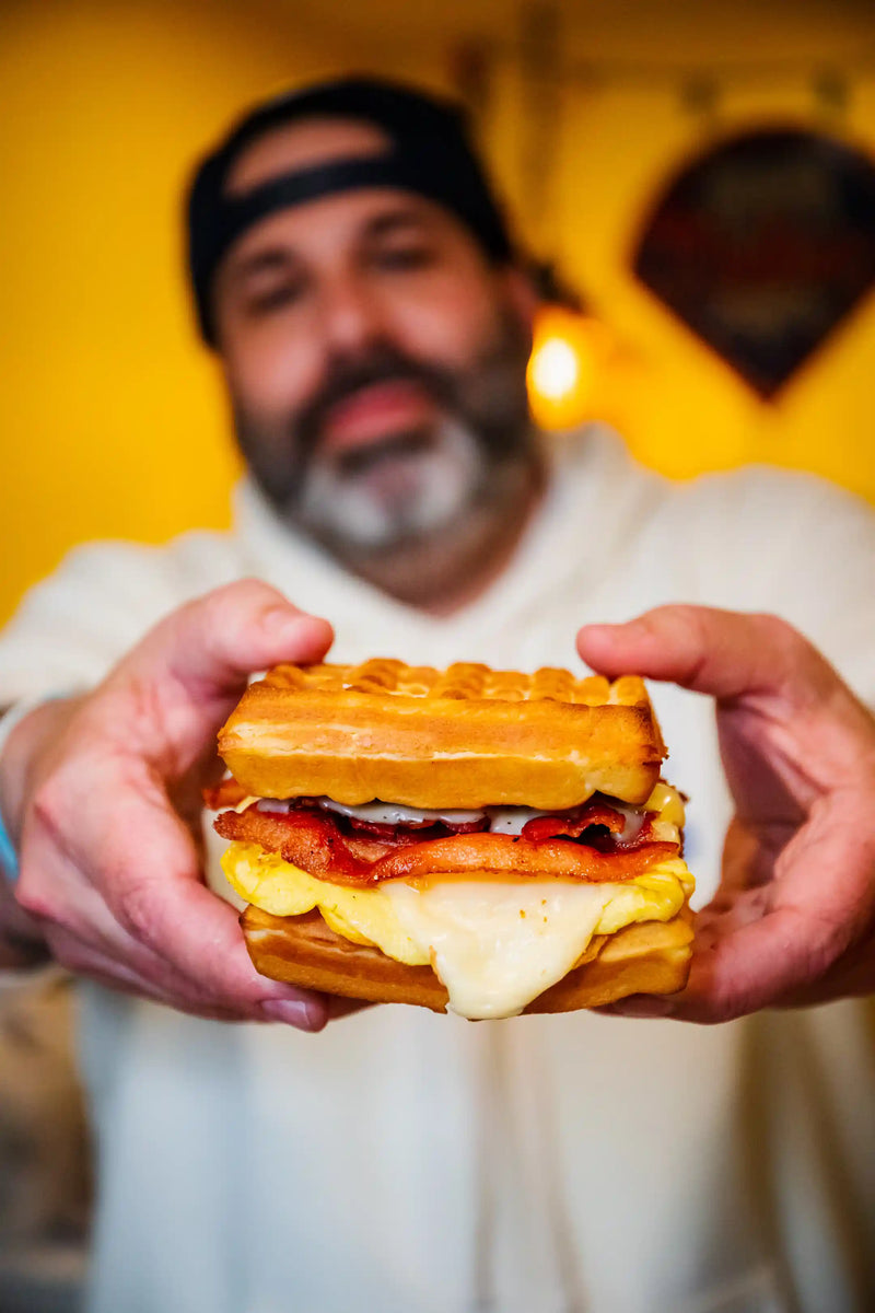 Person holding a waffle sandwich with a yellow background