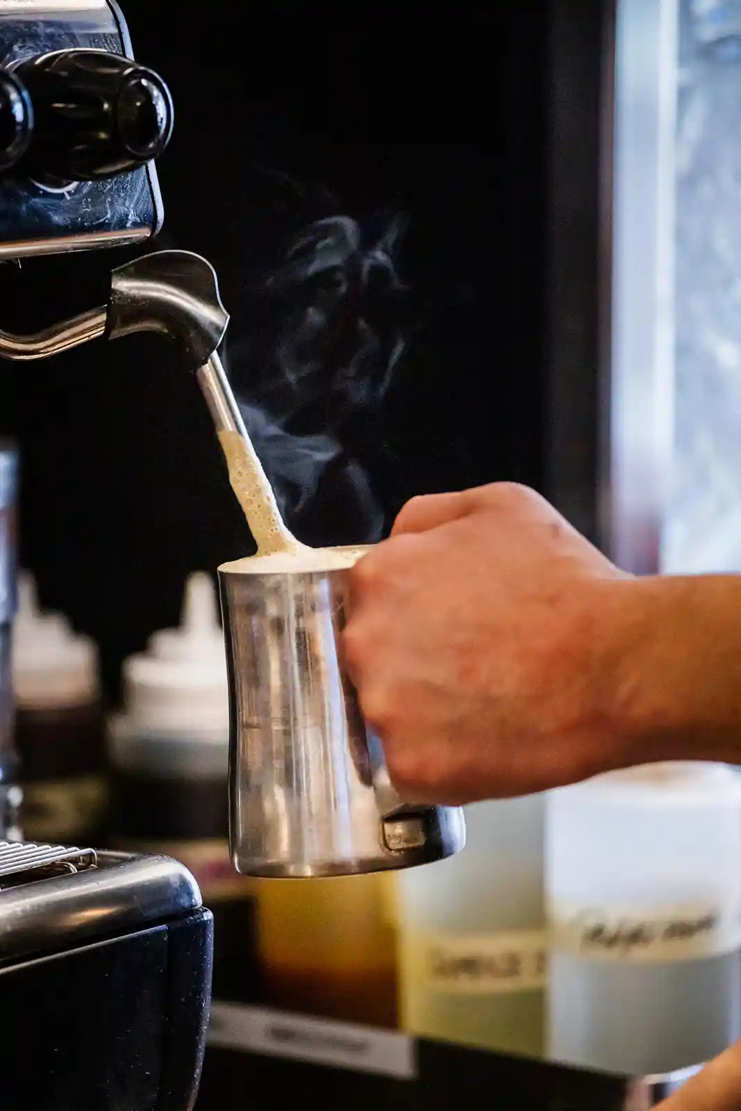 Person using a steam wand on an espresso machine with steam rising.