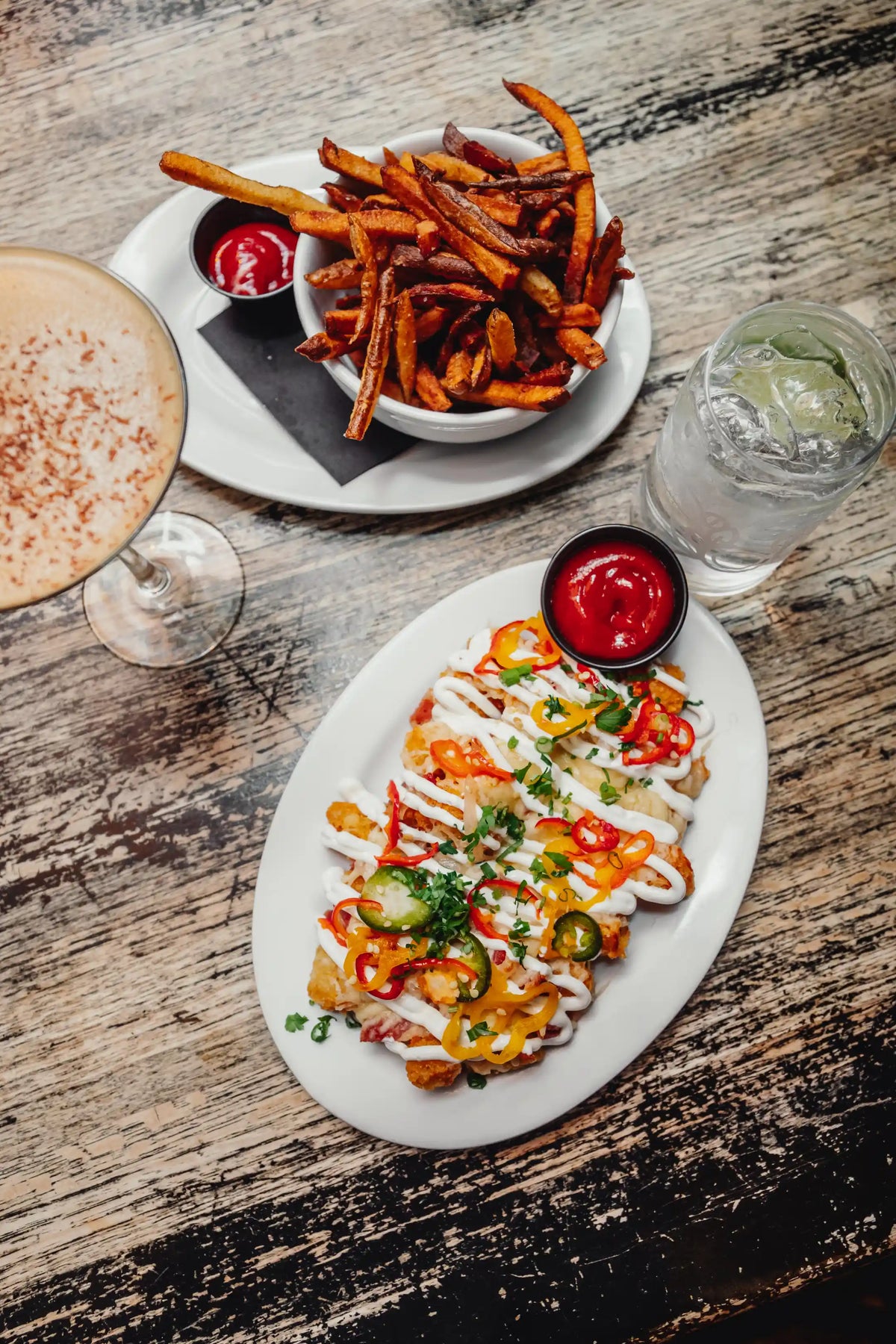 Plated dish of loaded nachos with a side of fries and drinks on a wooden table.