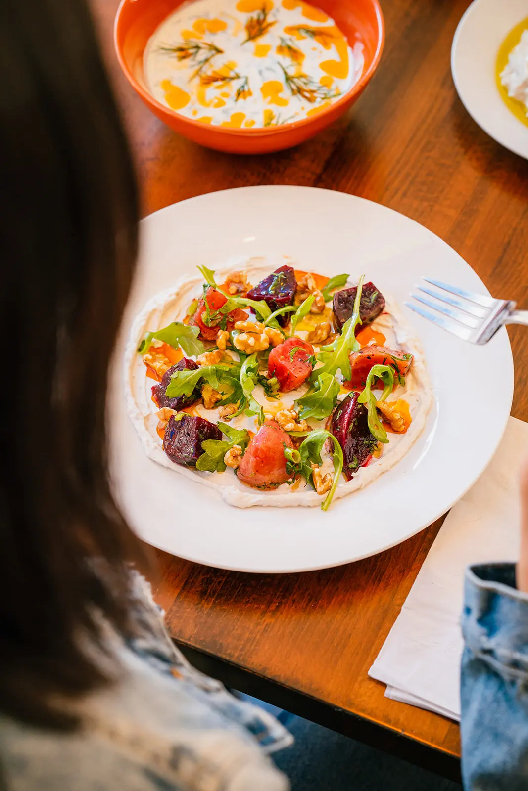 Woman eating Colorful salad with tomatoes, cucumbers, olives, and feta cheese on a white plate.