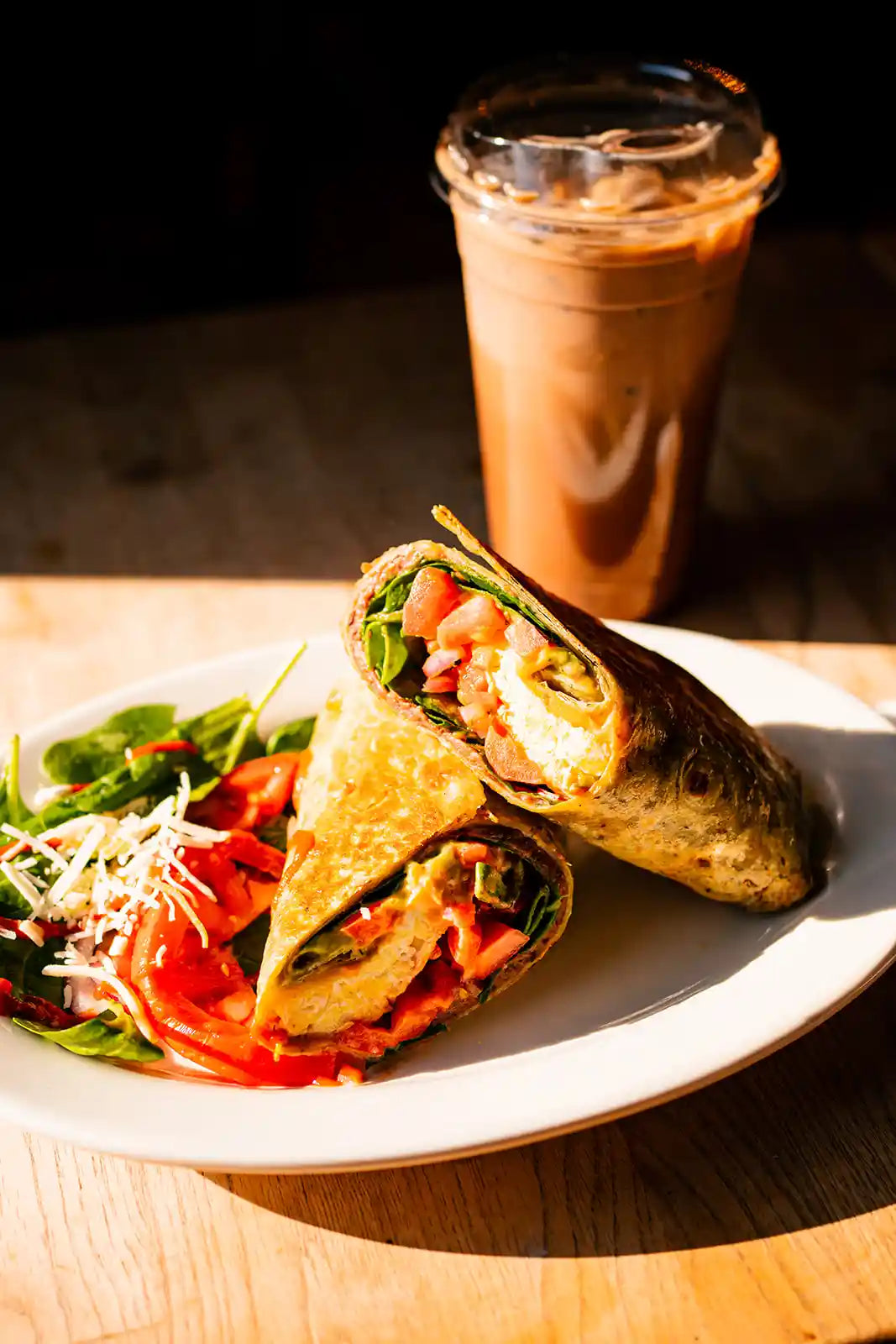 Breakfast wrap with salad and iced coffee on a wooden table