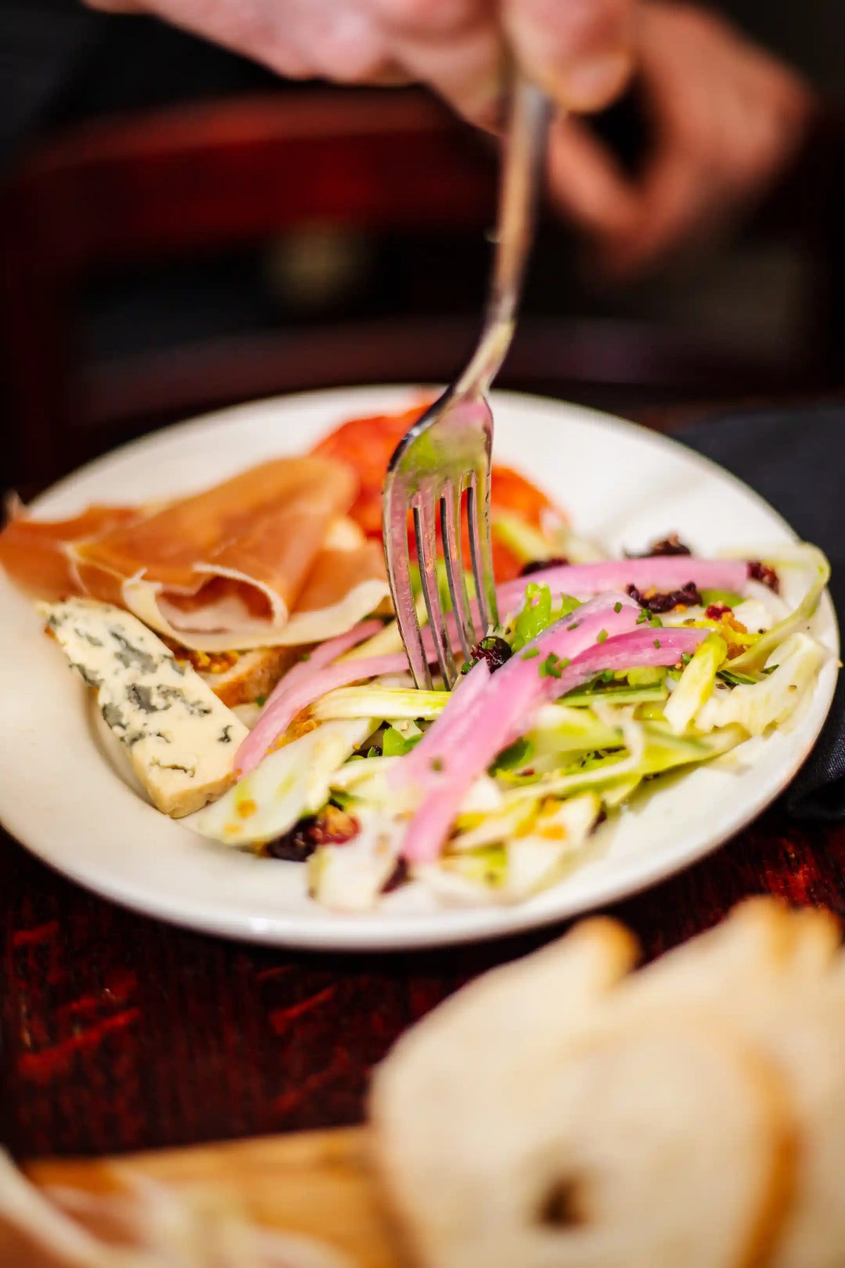 Close-up of a plate with salad and prosciutto, with a fork piercing a piece of salad.