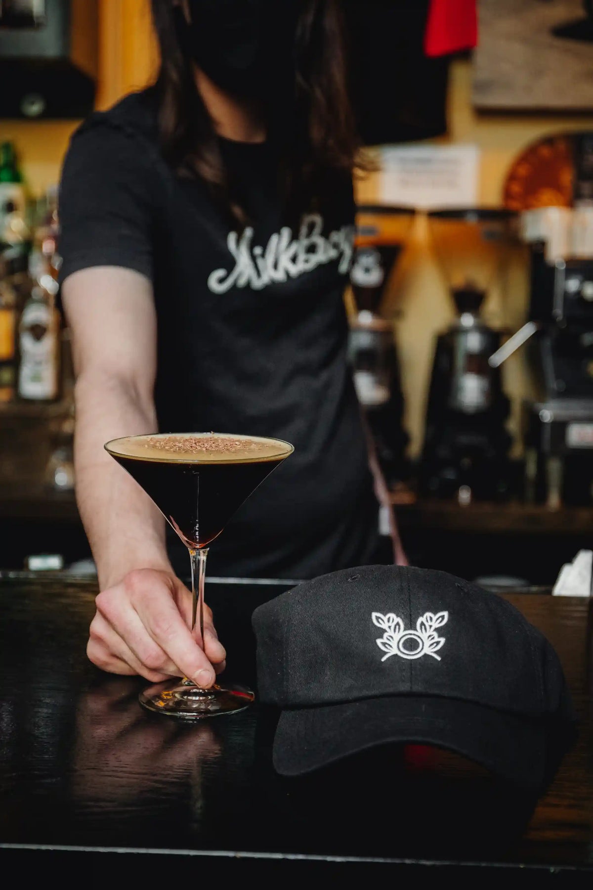 Person holding a Bean2Bean Espresso Martini with a blurred bar setting in the background
