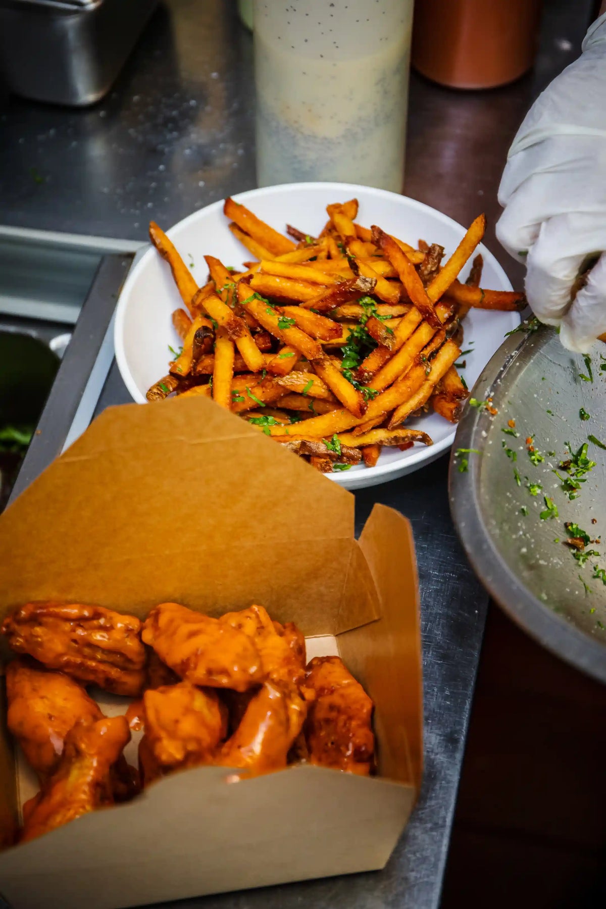Bowl of fries with a side of wings on a metal surface.