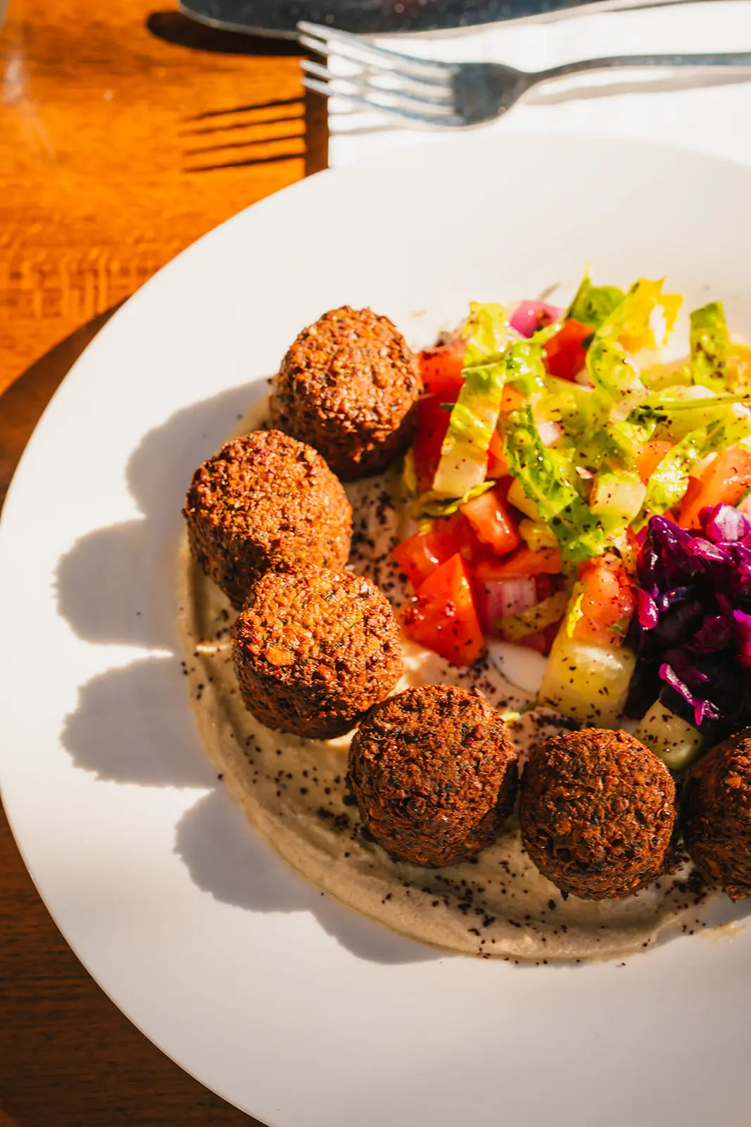 Plated falafel with a side salad on a white plate on a wooden table