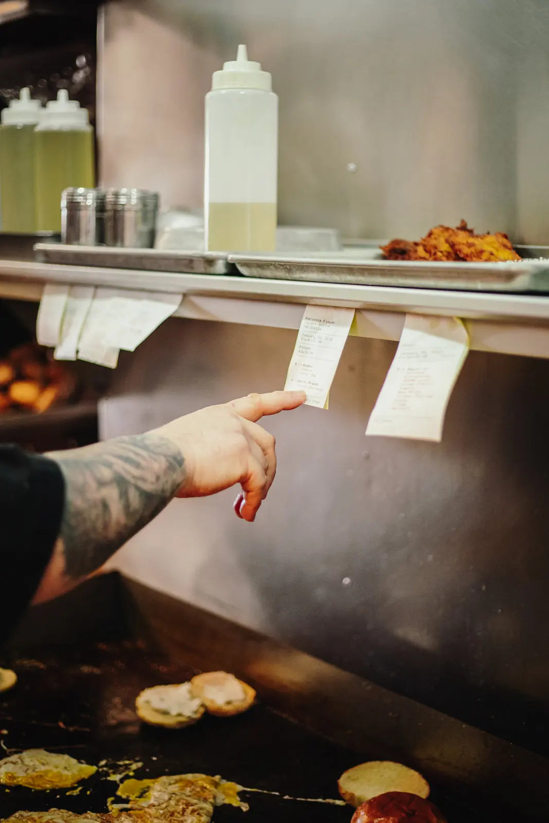 Person pointing at a menu or sign above a grill with food being cooked.
