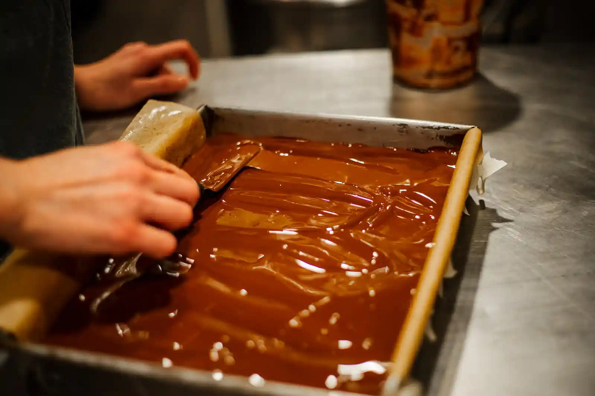 Person spreading chocolate in a baking tray with a spatula.