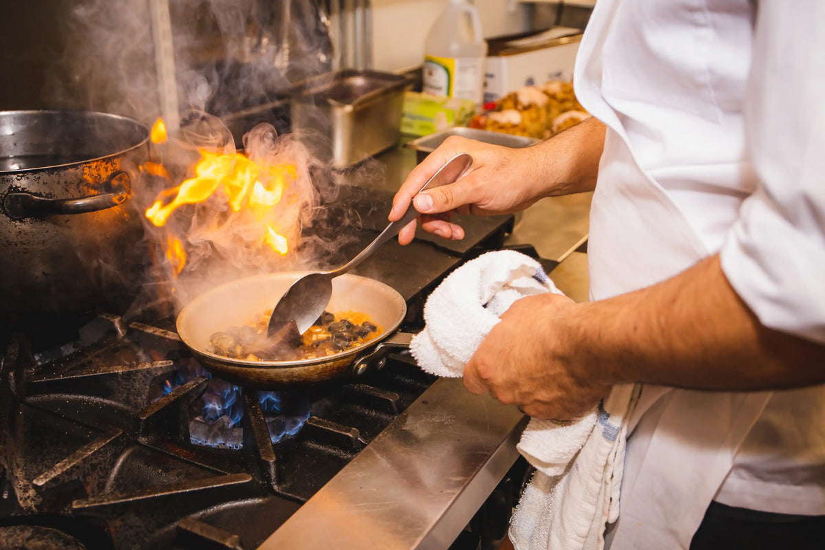 Chef cooking over high heat with flames in a professional kitchen