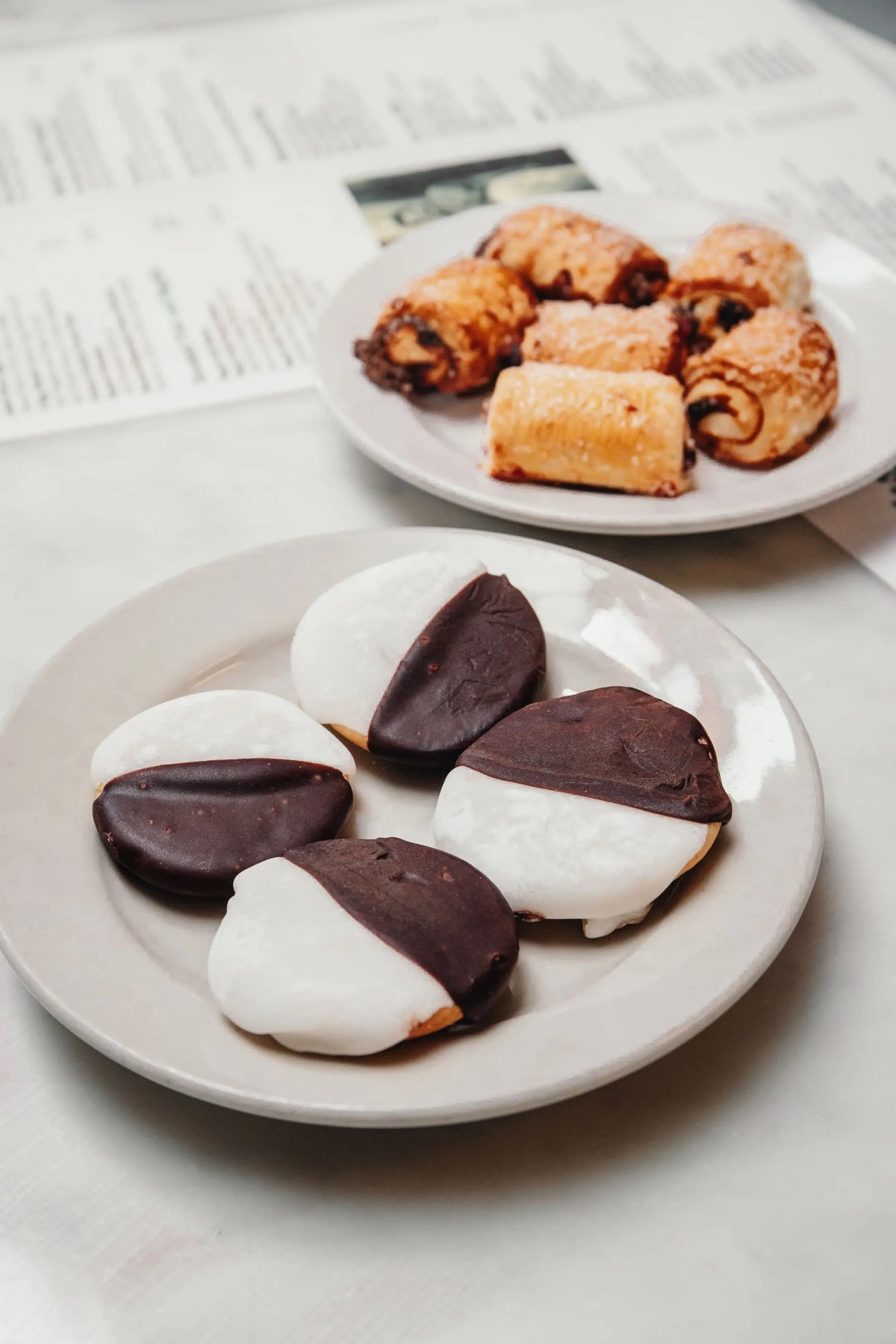 Two plates of black and white cookies on a newspaper background