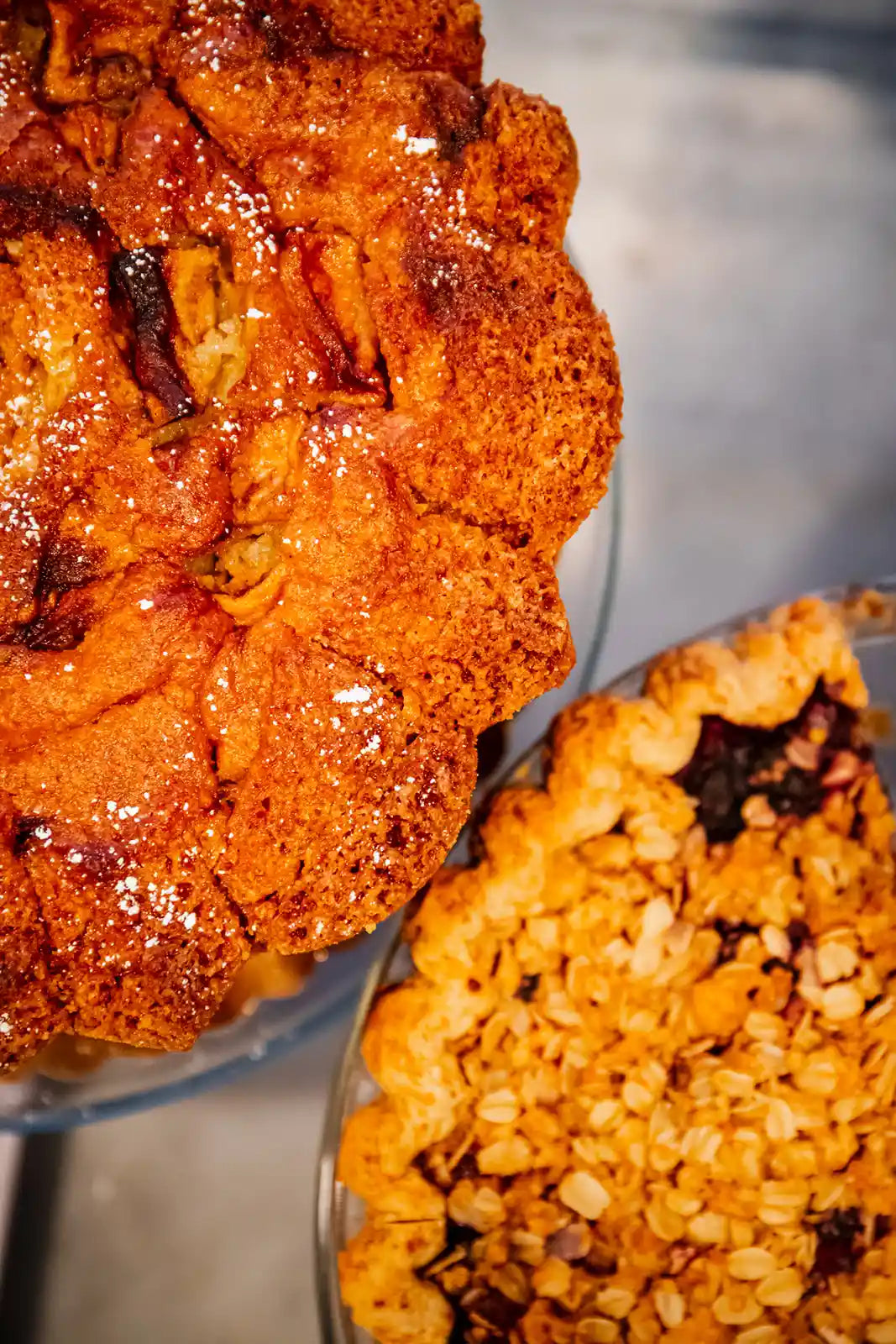 Two pies, one with a glistening top crust and the other with a textured surface, on a reflective surface.