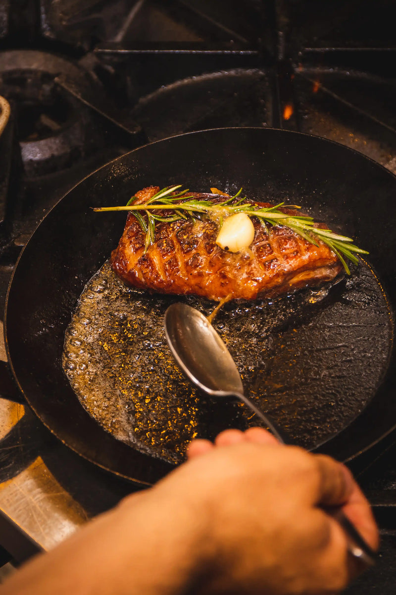 Salmon fillet with herbs being cooked in a pan on a stove.