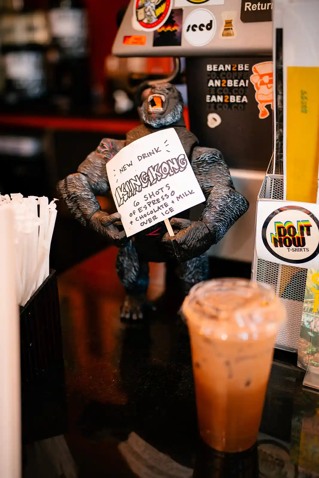 King Kong figurine holding a drink special card behind a coffee on a cafe counter