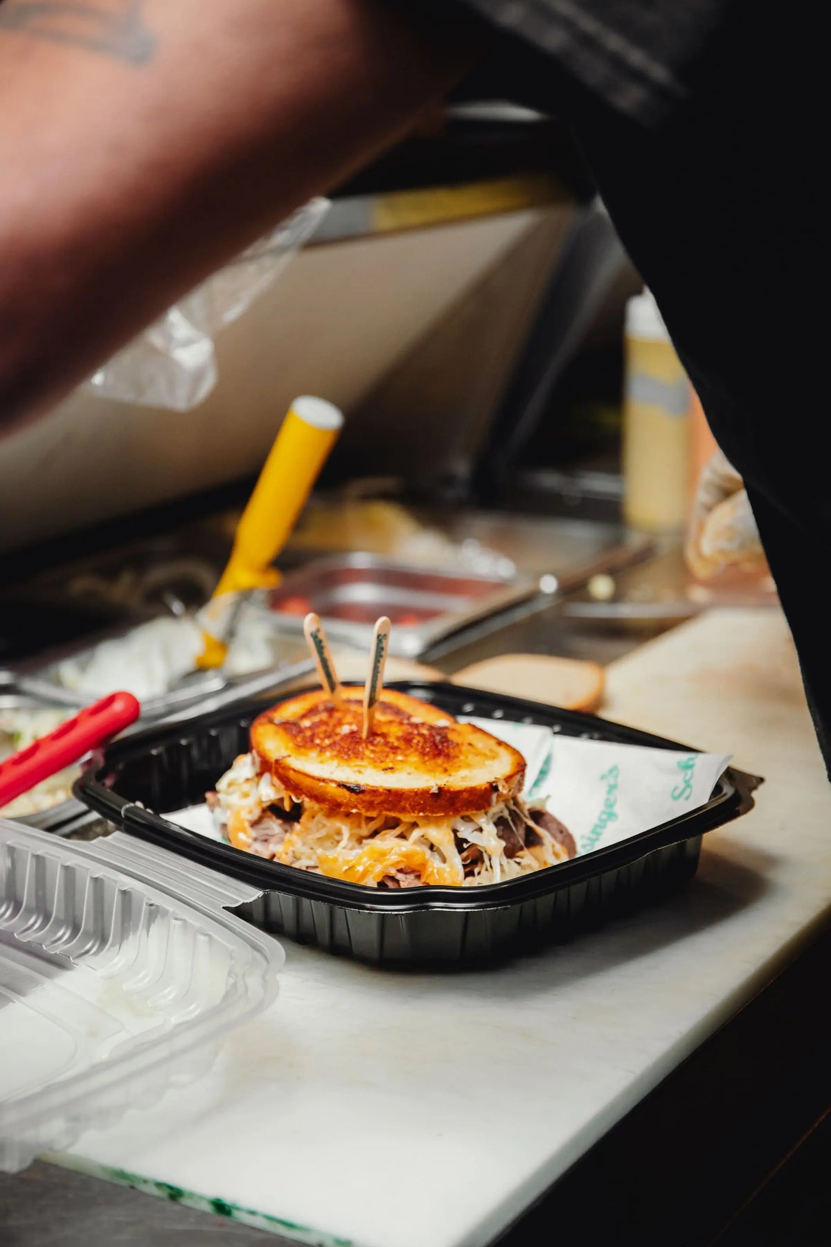 Close-up of a sandwich in a black container on a counter with a blurred background