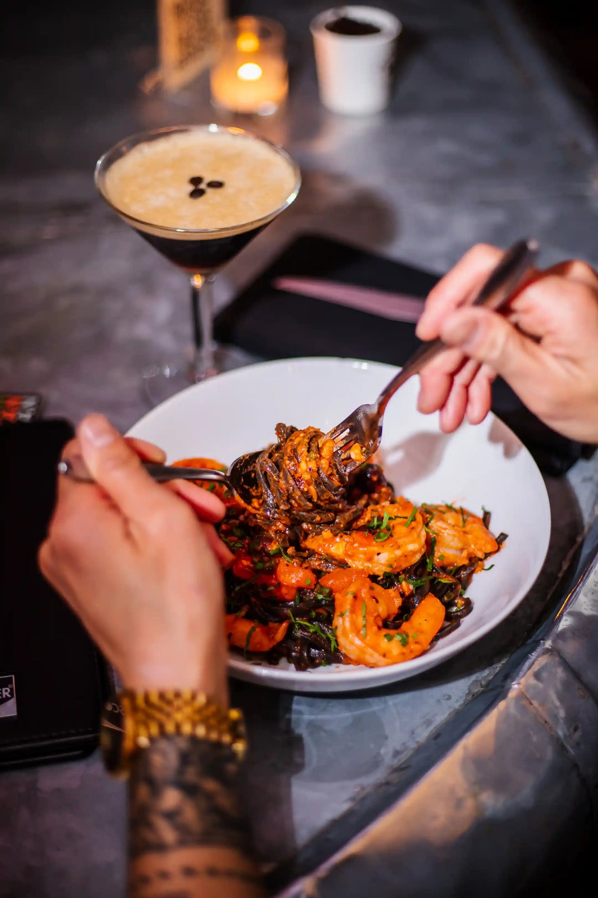 Person eating a plate of food, shrimp dish, with a cocktail in the background