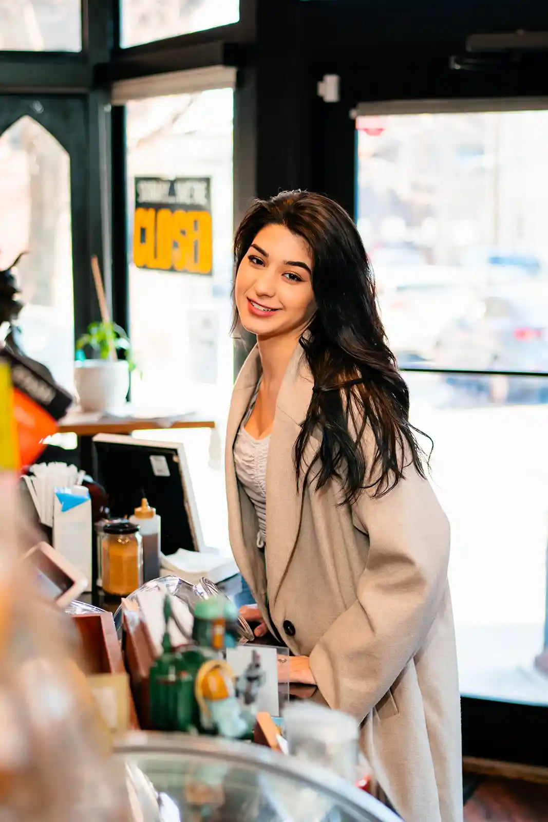 Woman standing in a cafe with a smile, surrounded by coffee cups and decor.