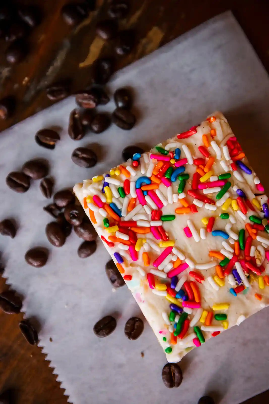 Square of white chocolateWhite frosted brownie sprinkles on a wooden surface with coffee beans.
