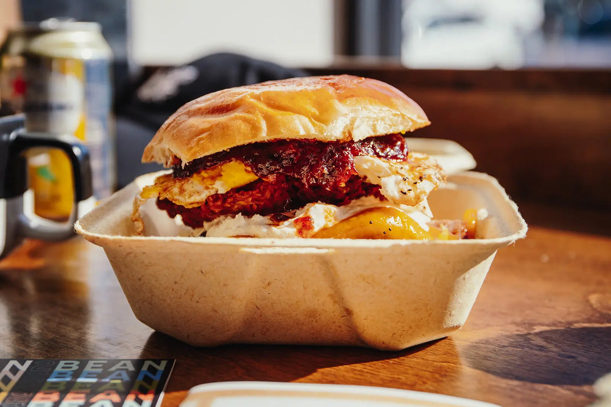 Burger in a cardboard container on a wooden table with a blurred background