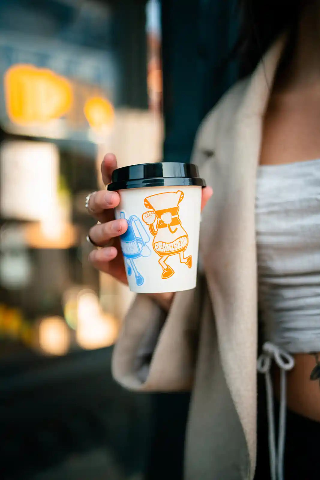 Person holding a coffee cup with Bean2Bean Coffee Co. stickers in an urban setting