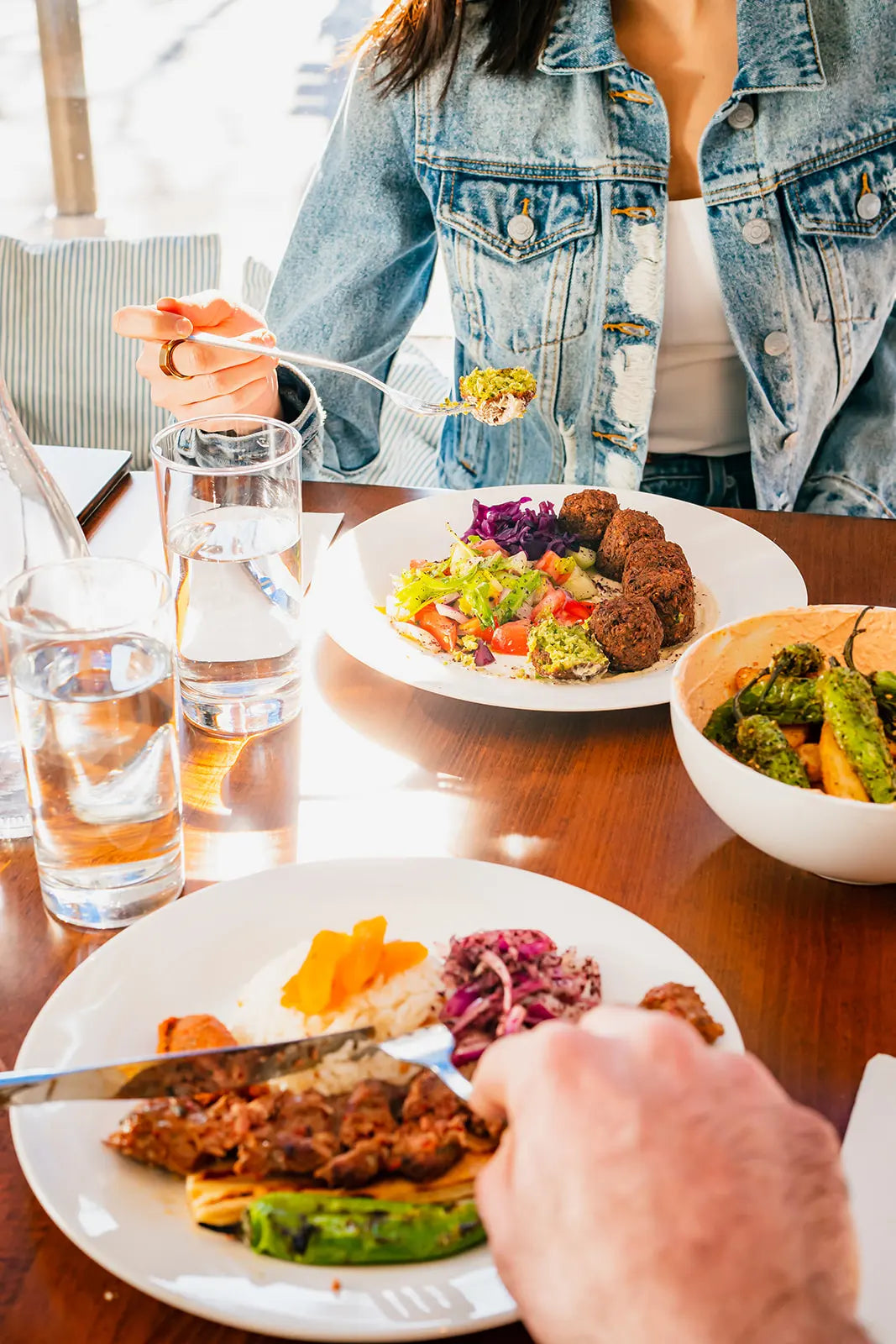 Person eating a meal with a focus on a plate of food and a glass of water.