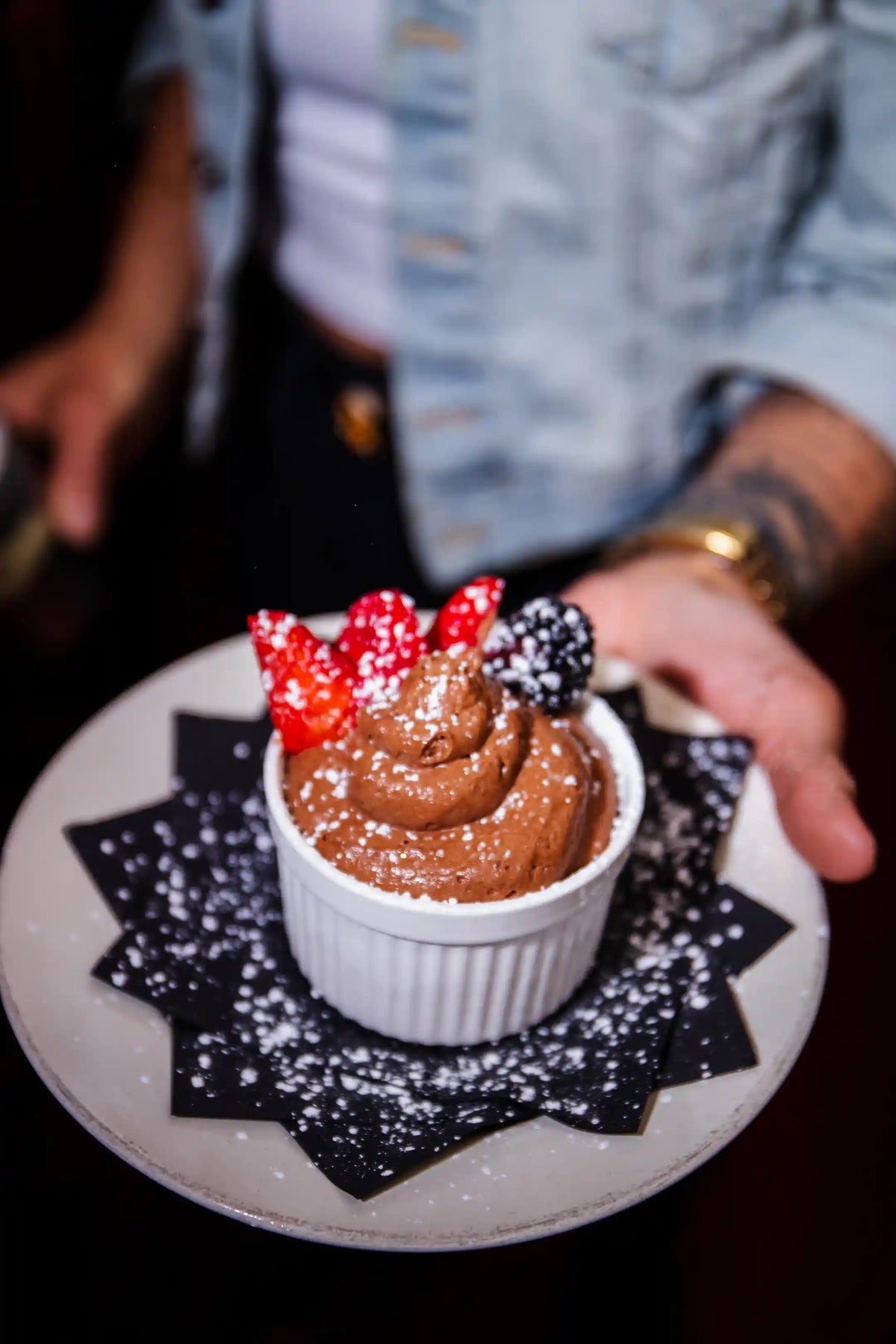 Chocolate dessert in a white bowl with red and black toppings on a decorative plate.
