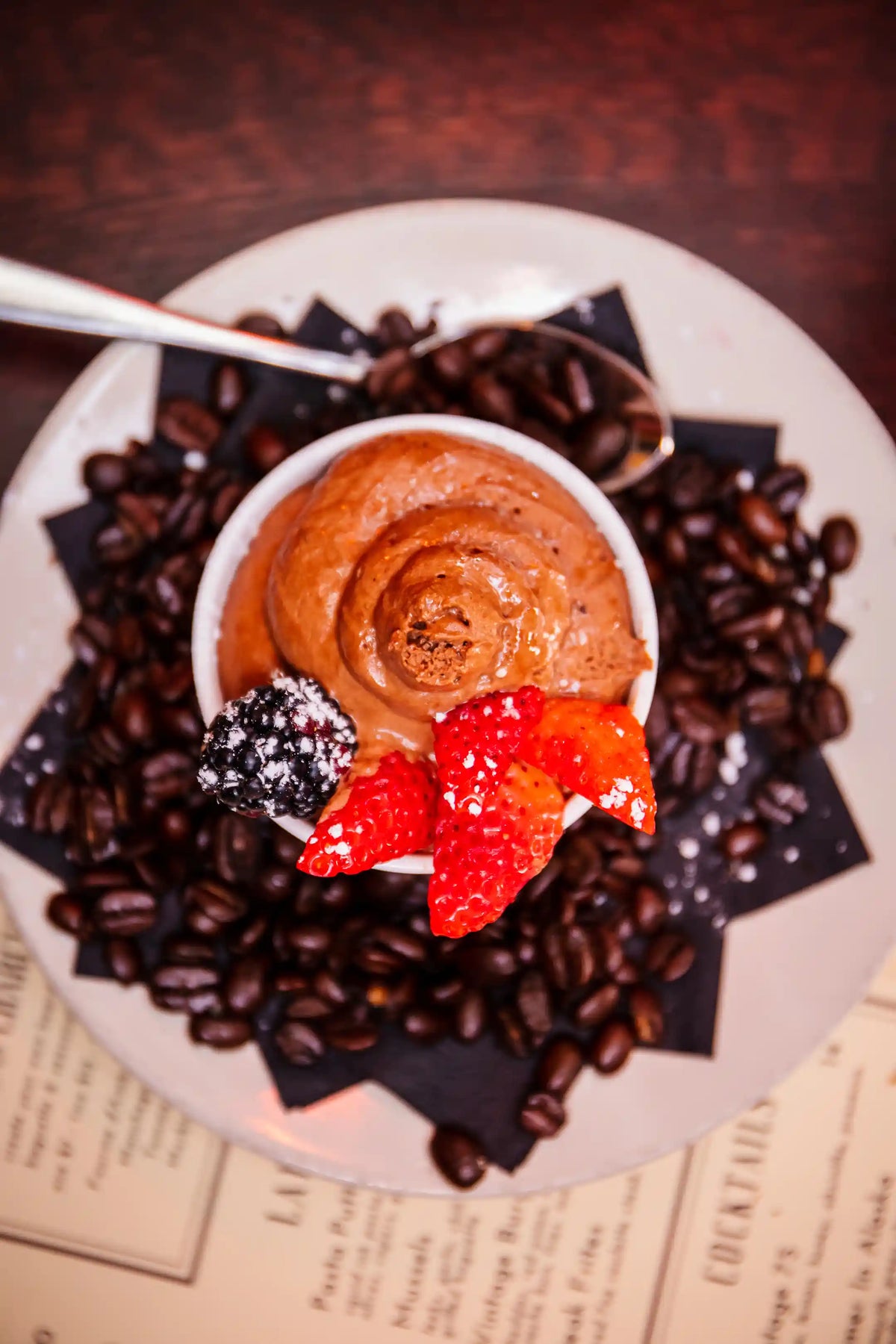 Dessert with a swirl of chocolate cream, berries, and coffee beans on a plate.