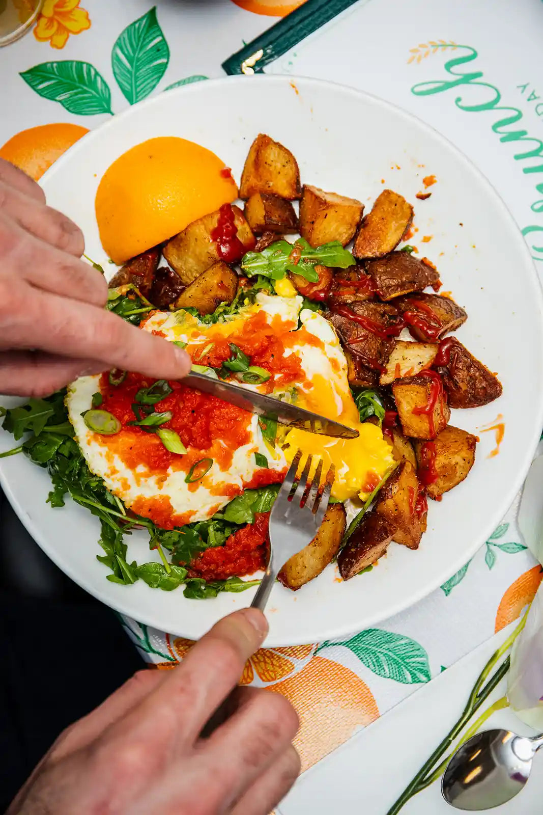 Plate of food with eggs, potatoes, and vegetables on a tablecloth with orange and green patterns.