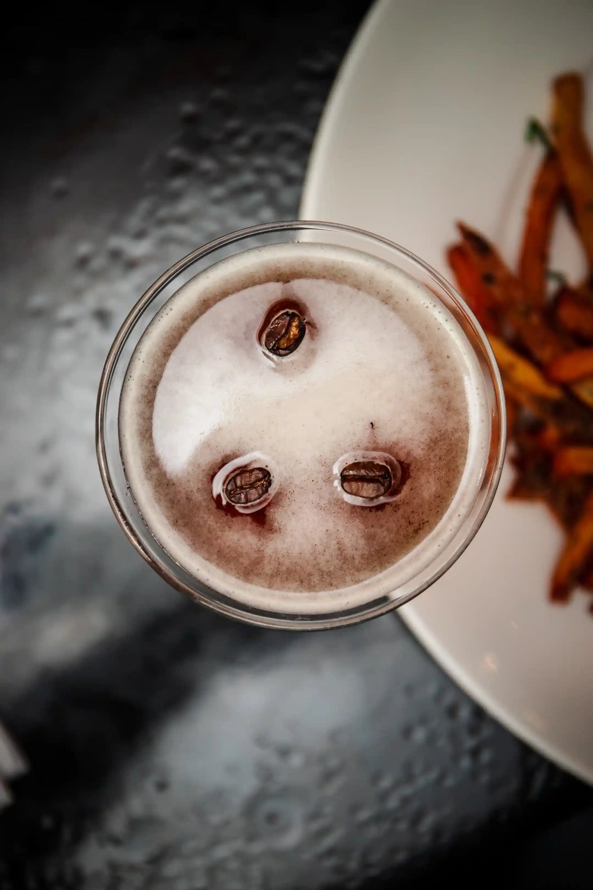 Espresso martini from above with floating coffee beans on a textured surface
