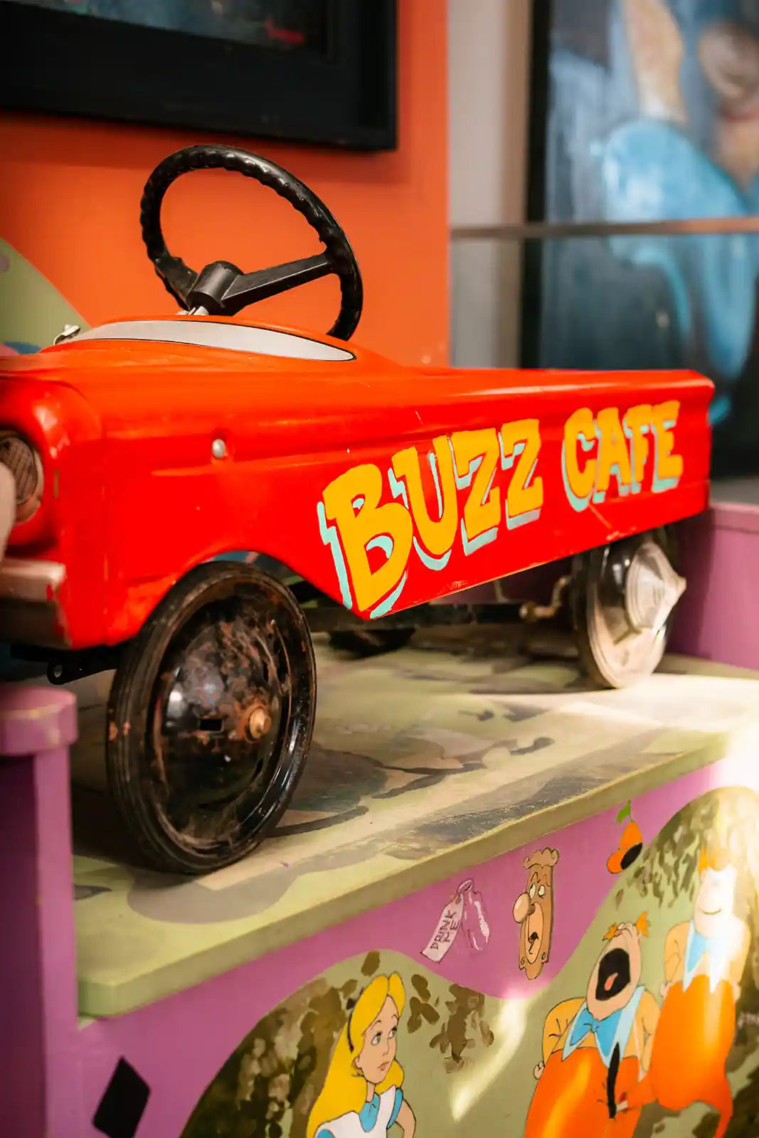 Red toy car with 'Buzz Cafe' branding on a pink surface with cartoon characters.
