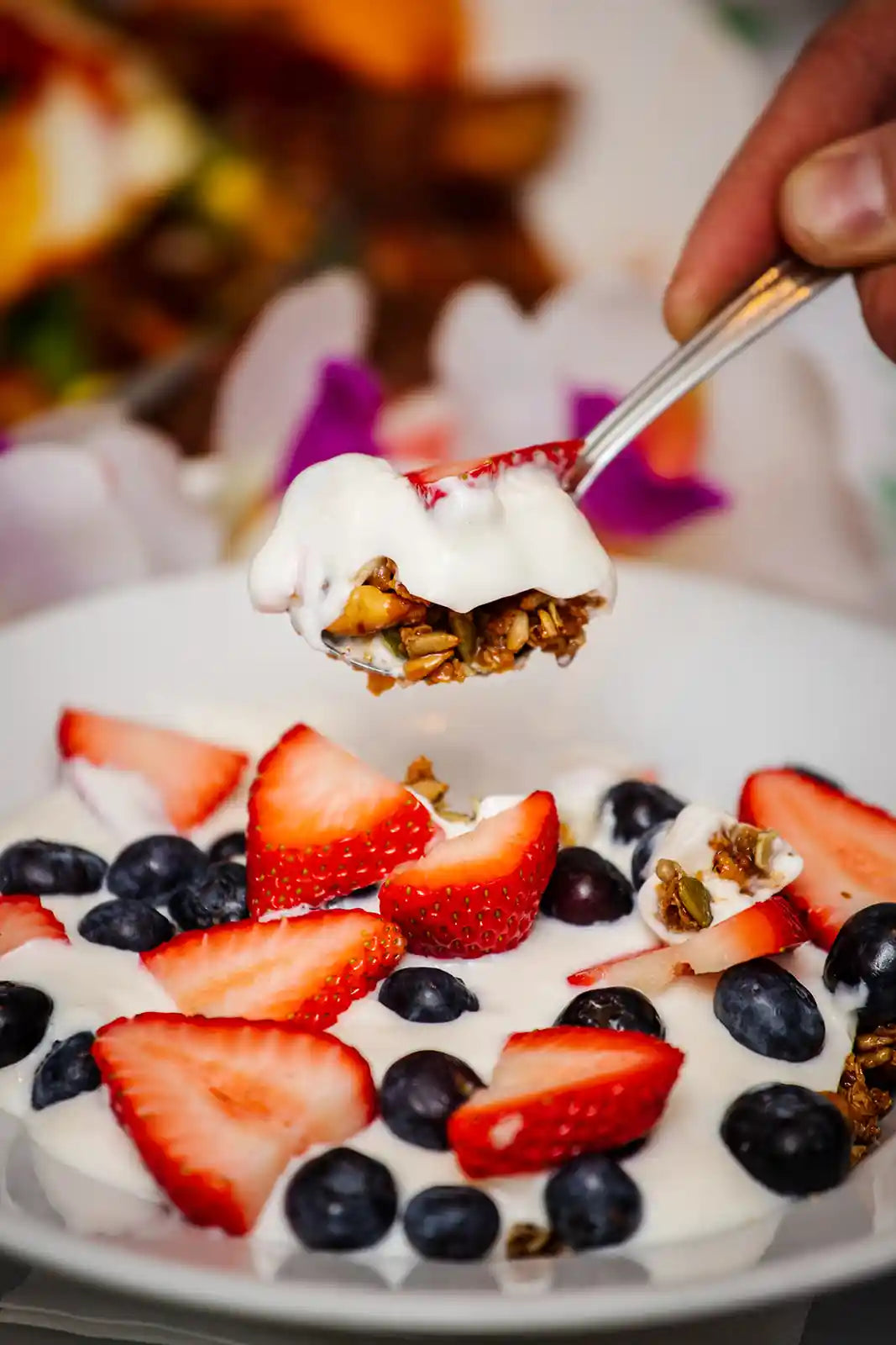 Yogurt with strawberries, blueberries, and granola being scooped with a spoon.
